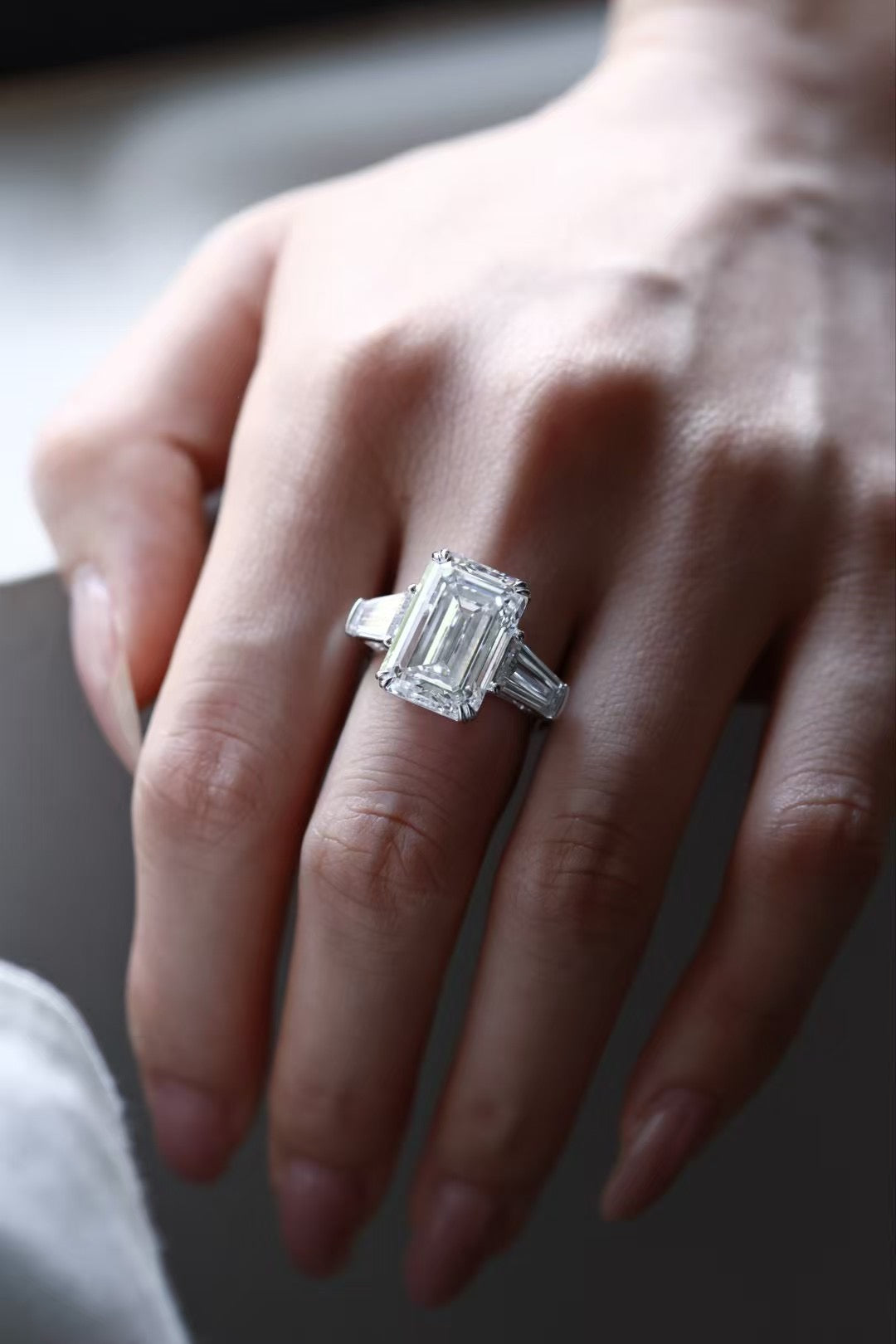Emerald-cut lab-grown diamond trilogy ring with tapered baguette side stones, worn on hand, view 4