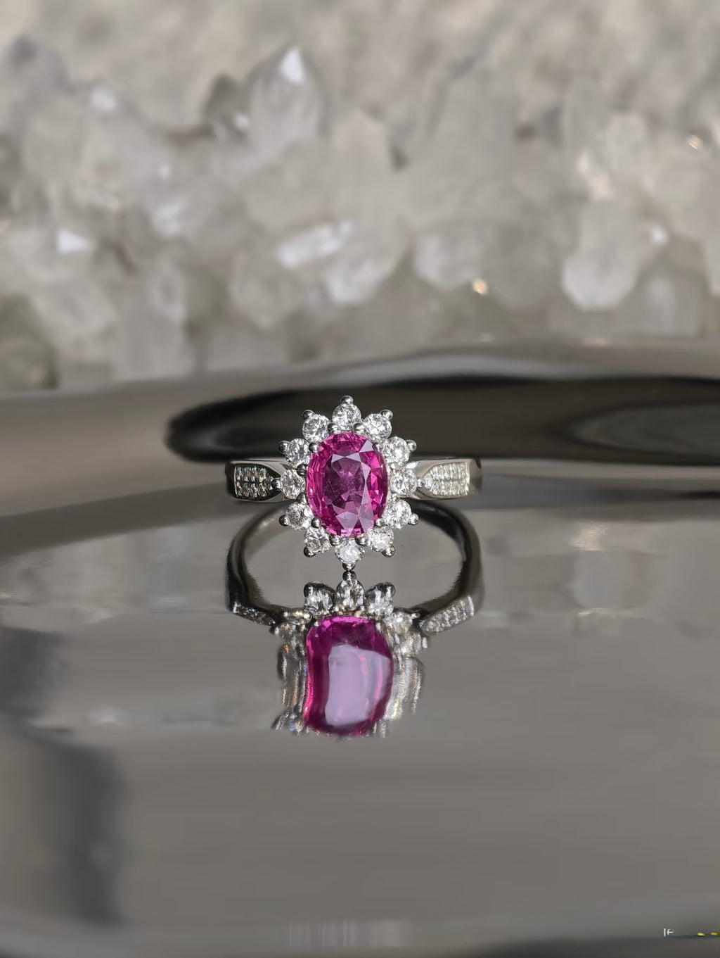 Pink sapphire halo ring on a reflective surface